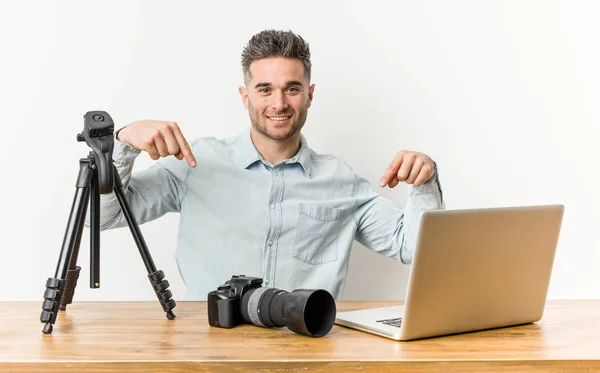 Young handsome photography teacher points down with fingers, positive feeling.