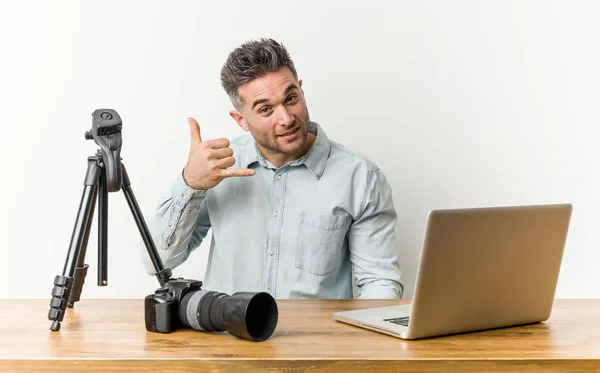 Young handsome photography teacher showing a mobile phone call gesture with fingers.