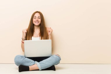 Genç zencefilkadın evinin zemin inde oturan yumruk yükselterek, mutlu ve başarılı hissediyorum. Zafer kavramı.