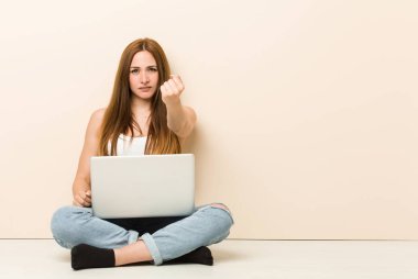 Evinin zemininde oturan genç zencefilli kadın kameraya yumruk göstererek, agresif yüz ifadesi.