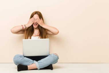 Evinin zemininde oturan genç zencefilli kadın elleri ile gözleri kaplıyor, geniş bir sürpriz bekliyor gülümsüyor.