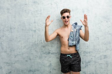 Havalı bilet tutan mayo giyen genç adam hoş bir sürpriz aldı, heyecanlı ve el kaldırarak.