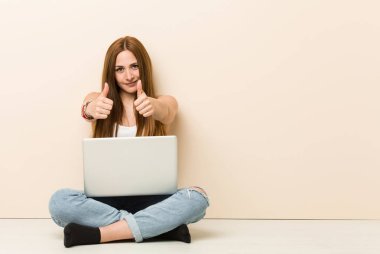 Genç zencefil kadın başparmak ups ile evinin zeminüzerinde oturan, bir şey hakkında tezahürat, destek ve saygı kavramı.