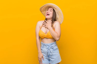 Genç beyaz kadın bir hasır şapka giyen, yaz bakmak yüksek sesle göğüs üzerinde el tutmak dışarı gülüyor.