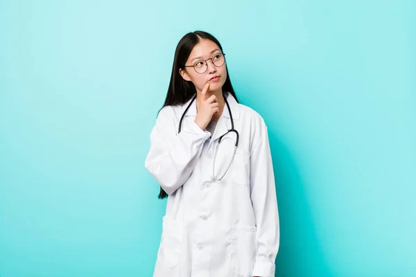 Young chinese doctor woman looking sideways with doubtful and skeptical expression.