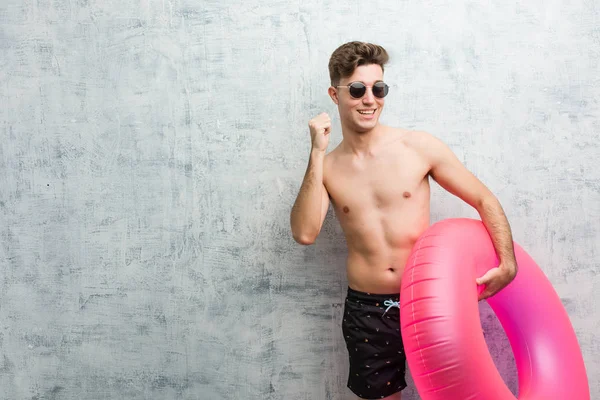 Pembe şişme çörek tutan genç adam dans eden ve eğlenen bir mayo giyiyor.