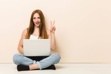 Genç zencefil kadın zafer işareti gösteren ve geniş gülümseyerek evinin katta oturan.