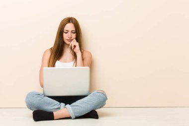 Genç zencefil kadın şüpheli ve şüpheci ifade ile yan bakarak evinin zeminüzerinde oturan.