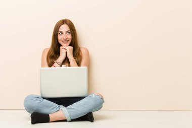 Evinin zemininde oturan genç zencefilli kadın ellerini çenenin altında tutuyor, mutlu bir kenara bakıyor.