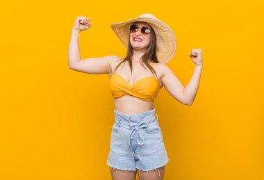 Hasır şapka takan genç beyaz kadın, yaz görünümü nde kollarla güç jesti gösteren, kadınsı gücün sembolü