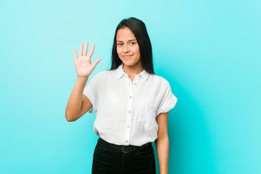 Mavi bir duvara karşı genç İspanyol Cool kadın parmak ile beş numara gösteren neşeli gülümseyen.