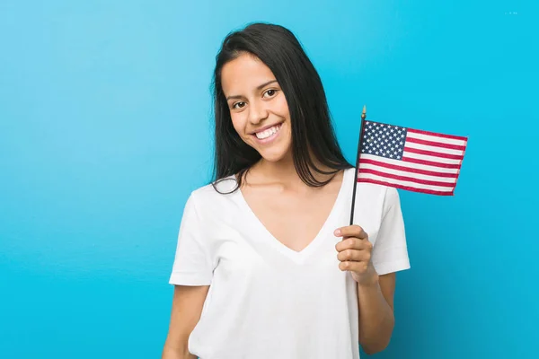 Young hispanic woman holding a united states flag happy, smiling and cheerful.