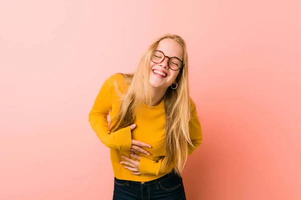 Adorable teenager woman laughs happily and has fun keeping hands on stomach.