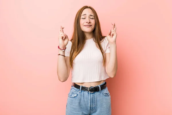 幸運を持っているために指を横切るピンクの壁に対する若い赤毛の生姜の女性 — ストック写真