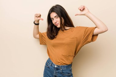 Bej bir arka plan karşı genç esmer kadın gururlu ve kendine güvenen, örnek takip hissediyor.