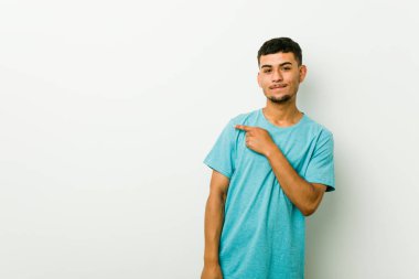 Genç İspanyol adam gülümseyen ve kenara işaret, boş uzayda bir şey gösteren.