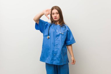 Beyaz bir duvara karşı genç hemşire kadın bir nefret jest gösteren, thumbs Down. Anlaşmazlık konsepti.