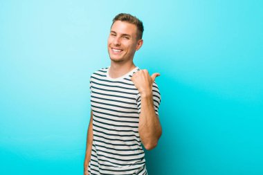 Başparmak parmak uzakta mavi bir duvara karşı genç beyaz adam, gülme ve kaygısız.