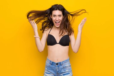 Bir zafer veya başarı kutluyor sarı arka plan karşı bir bikini giyen genç esmer kadın, o sürpriz ve şok.