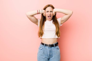 Çok yüksek ses duymamaya çalışan elleri ile kulakları kaplayan pembe bir duvara karşı genç kızıl saçlı zencefil kadın.