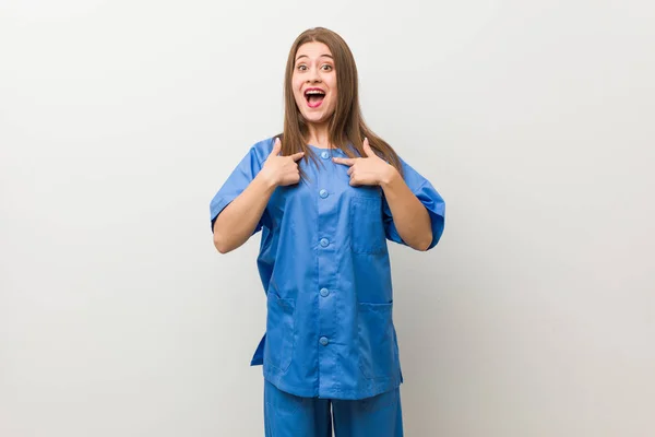Νεαρή Νοσοκόμα Γυναίκα Ένα Λευκό Τοίχο Έκπληκτος Δείχνοντας Δάχτυλο Χαμογελαστά — Φωτογραφία Αρχείου