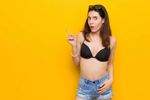 Młoda Brunetka Kobieta Ubrana Bikini Przeciwko Żółtym Tle Wskazując Bok — Zdjęcie stockowe