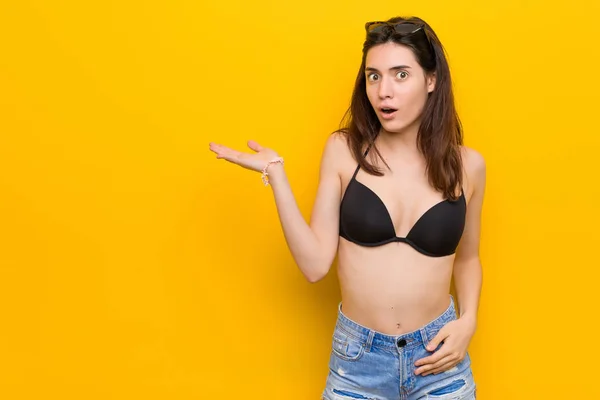 Młoda Brunetka Kobieta Ubrana Bikini Przeciwko Żółtym Tle Wrażeniem Posiadania — Zdjęcie stockowe