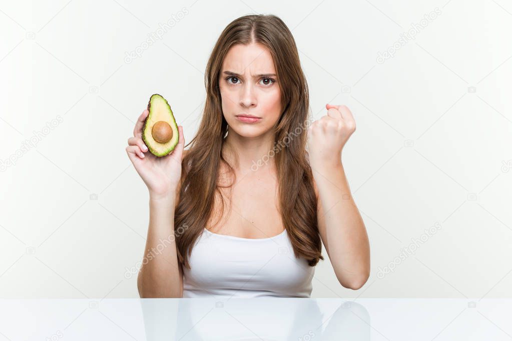 Young caucasian woman holding an avocado showing fist to camera, aggressive facial expression.
