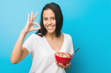 Genç İspanyol kadın bir tahıl kase neşeli ve emin ok jest gösteren tutan.