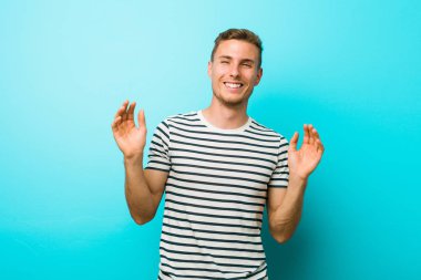 Mavi duvara karşı genç beyaz adam sevinçli bir kahkaha çok gülüyor. Mutluluk kavramı.