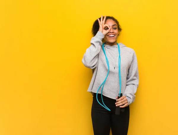 Young fitness black woman confident doing ok gesture on eye. Holding a jump rope.