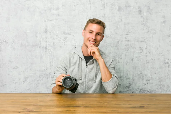 Jovem Fotógrafo Segurando Uma Câmera Uma Mesa Sorrindo Feliz Confiante — Fotografia de Stock