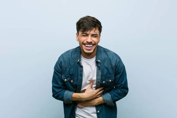 Young hispanic cool man laughs happily and has fun keeping hands on stomach.