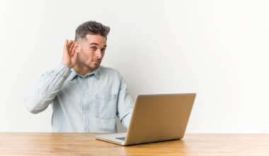 Genç yakışıklı adam bir dedikodu dinlemeye çalışırken onun laptop ile çalışıyor.