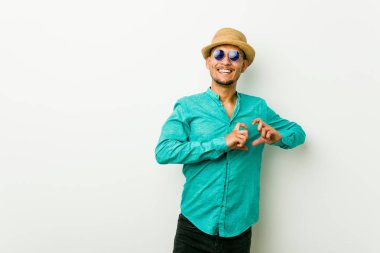 Genç İspanyol adam gülümseyerek bir yazlık giysiler giyen ve elleri ile bir kalp şekli gösteren.