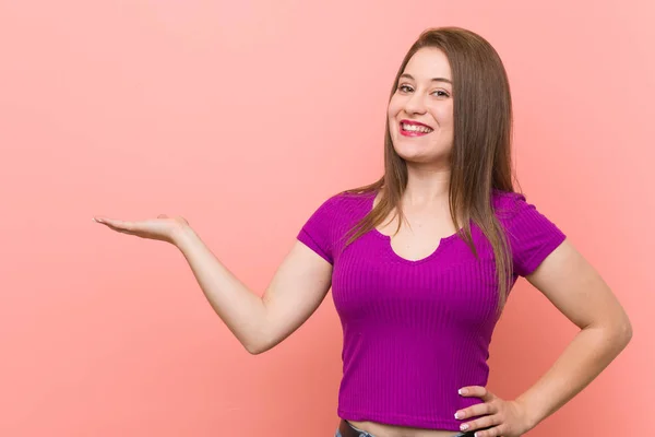 手のひらにコピースペースを示し 腰に別の手を保持するピンクの壁に対する若いヒスパニックの女性 — ストック写真