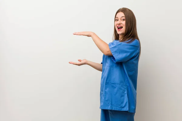 Jonge Verpleegster Vrouw Tegen Een Witte Muur Geschokt Verbaasd Houden — Stockfoto