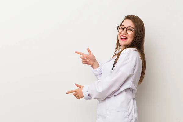 Jonge Dokter Vrouw Tegen Een Witte Muur Opgewonden Wijzend Met — Stockfoto
