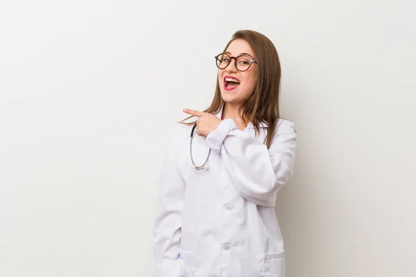 Jonge Dokter Vrouw Tegen Een Witte Muur Glimlachend Wijst Opzij — Stockfoto