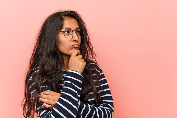 Young intellectual indian woman looking sideways with doubtful and skeptical expression.