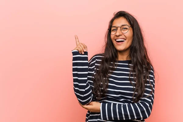 Young intellectual indian woman smiling cheerfully pointing with forefinger away.