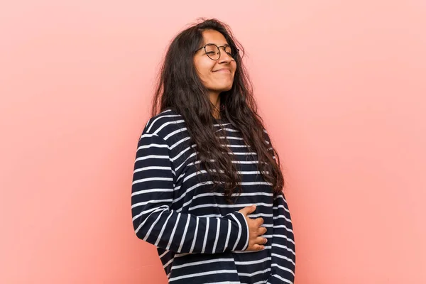 Young intellectual indian woman touches tummy, smiles gently, eating and satisfaction concept.