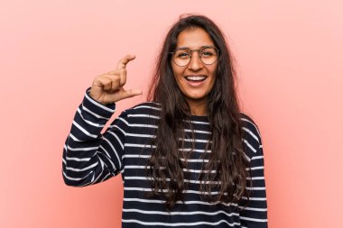 Genç entelektüel hintli kadın ön parmakları ile küçük bir şey tutan, gülümseyen ve kendinden emin.