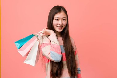 Bir alışveriş çantası tutan genç asyalı kadın mutlu, gülümseyen ve neşeli.