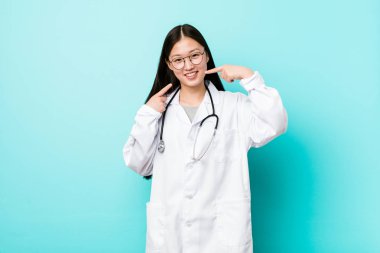 Genç Çinli doktor kadın gülümsüyor, ağızda parmaklarını işaret.