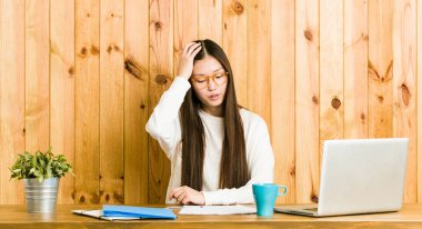 Masasında okuyan genç Çinli kadın yorgun ve çok uykulu başını el tutmak.