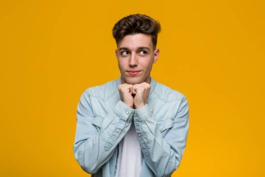 Denim gömlek giyen genç yakışıklı öğrenci çene altında ellerini tutar, bir kenara mutlu bakıyor.