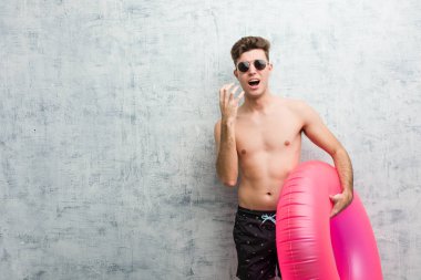 Pembe şişme çörek tutan genç adam öfkeyle çığlık atan bir mayo giyiyor.