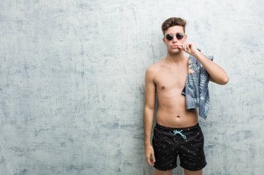 Dudaklarında parmakları yla mayo giyen genç beyaz adam sır tutuyor.