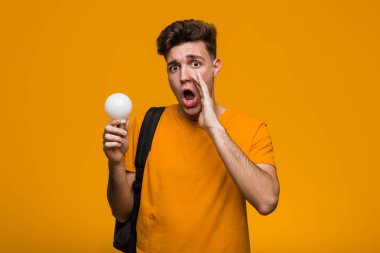 Genç öğrenci bir ampul tutan neşeyle işaret parmağı ile işaret gülümseyerek uzakta.